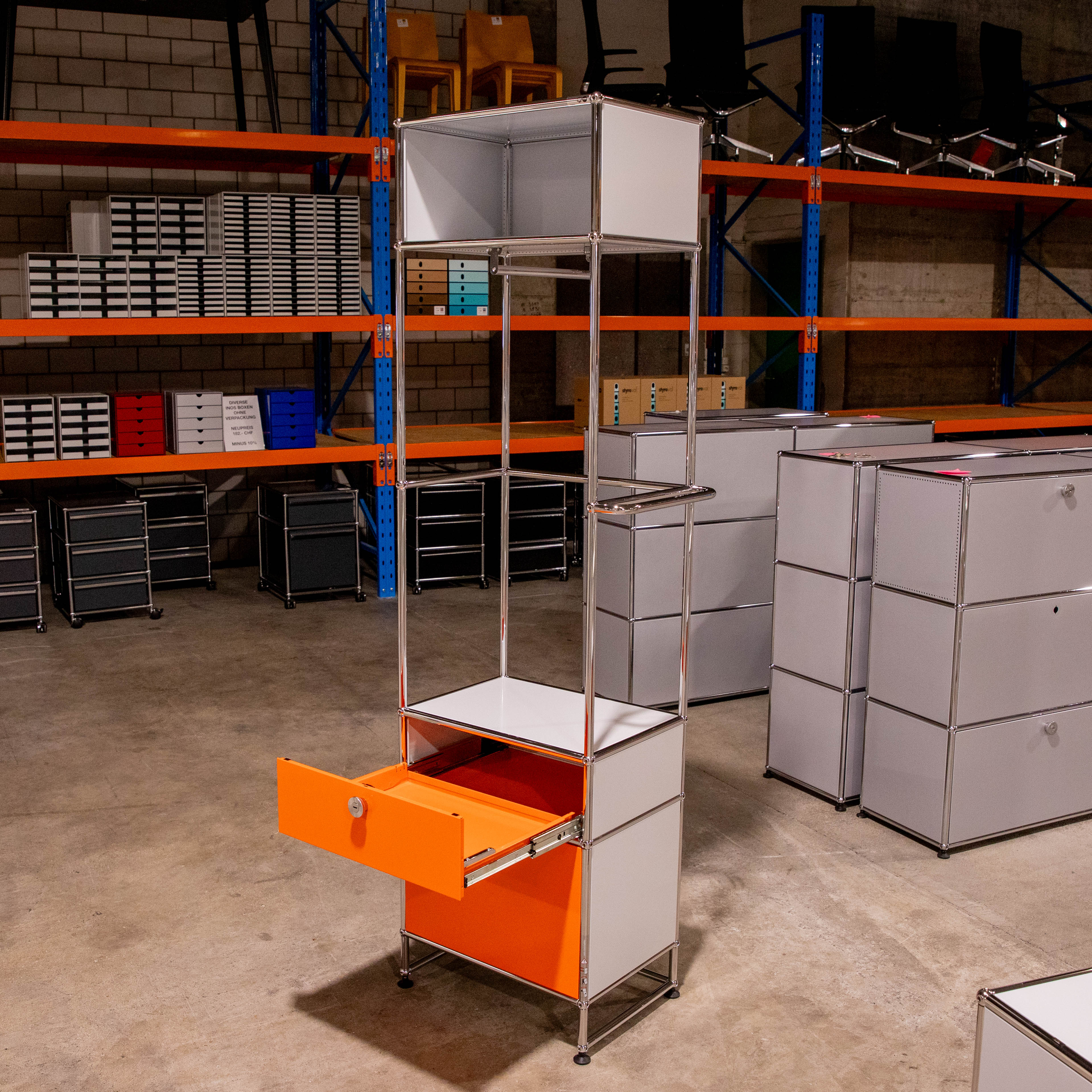 Hohe, gebrauchte USM Haller Garderobe in Lichtgrau/Orange im Lager. Mit offenem Fach oben, geschlossenem Fach, Kleiderstange mit Bügel und orangefarbener Ausziehtüre unten leicht geöffnet. Leichte Gebrauchsspuren.