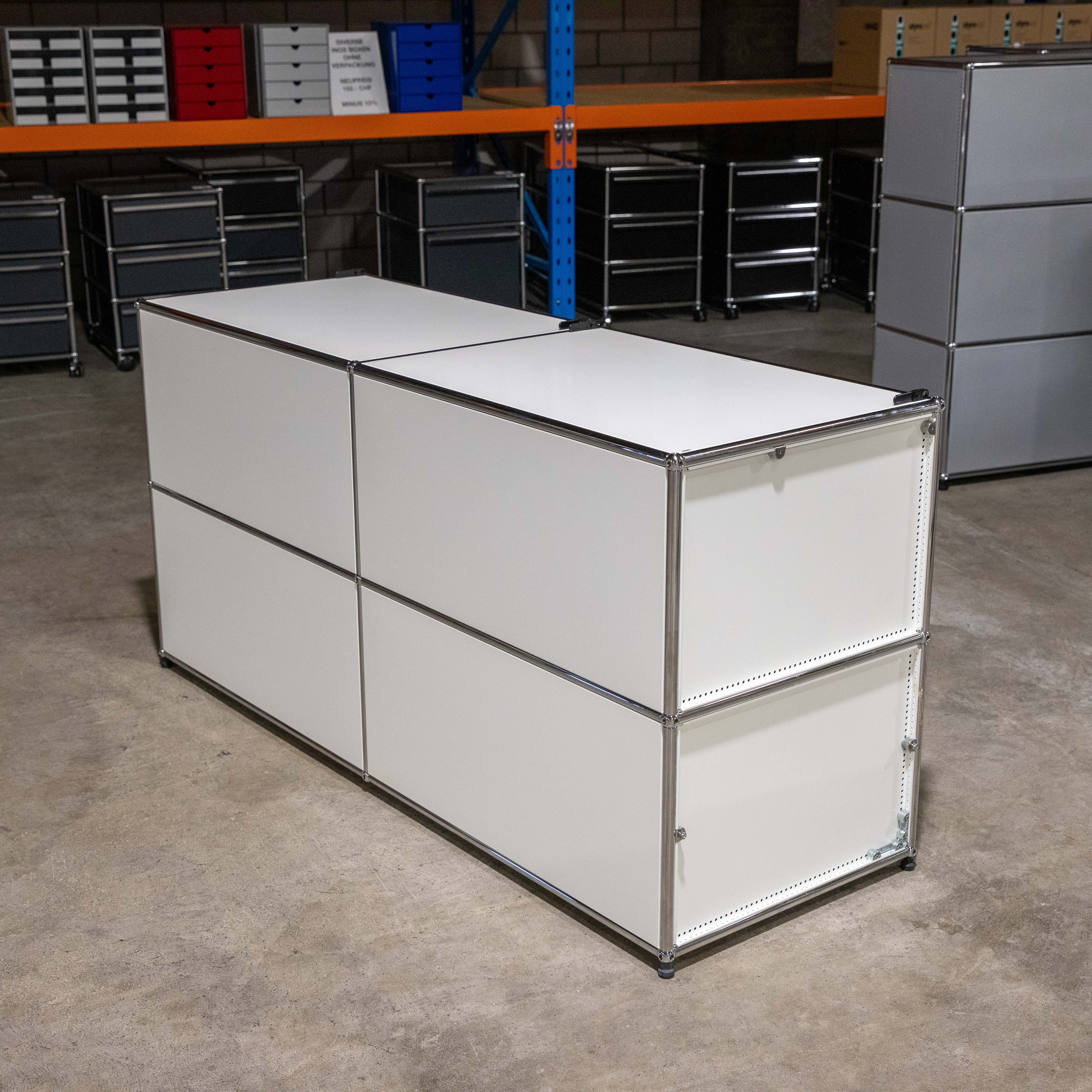 USM Haller Sideboard in Weiß/Lichtgrau, 4 Module (2 breit, 2 hoch) mit verchromtem Stahlrohrrahmen. Weiße Fronten, 1 lichtgraue Klapptür, linke Außenwand gelocht. Gebraucht mit deutlichen Gebrauchsspuren.
