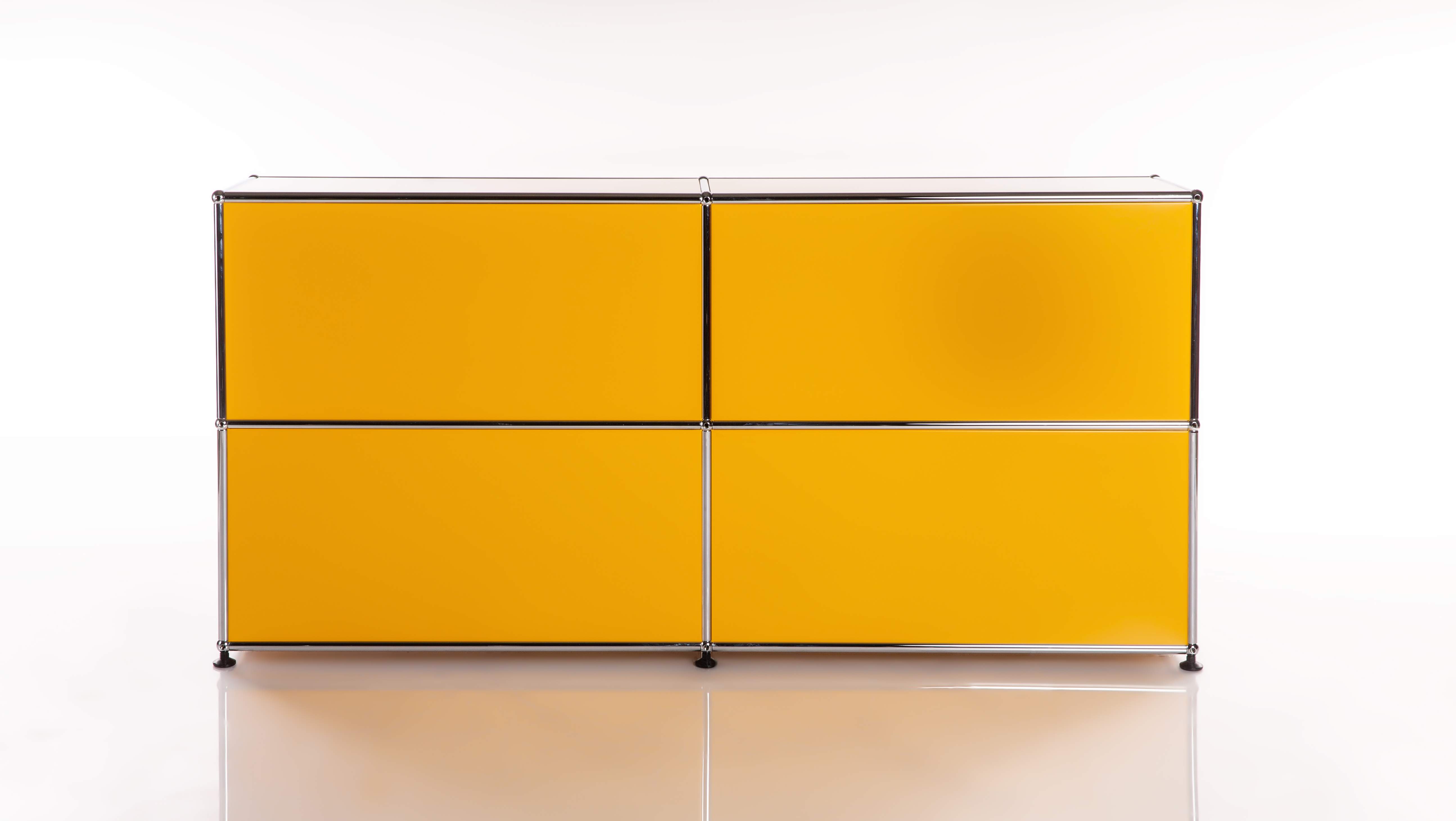 Credenza modulare giallo brillante con 4 scomparti quadrati in griglia 2x2. Struttura in tubi metallici cromati lucidi e giunti a sfera. Su piano bianco riflettente davanti a sfondo bianco semplice.