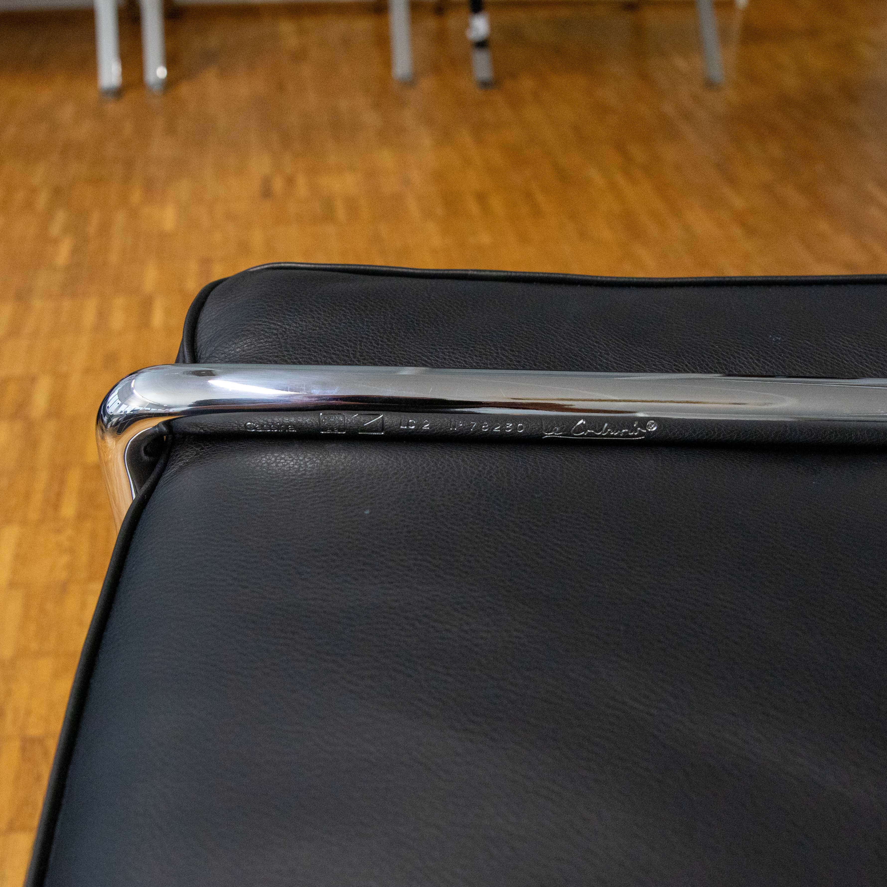 A close-up of the polished chrome tube on a Le Corbusier LC2 leather armchair, directly above the black upholstery. A clear engraving on the frame reads ‘Cassina LC2 N° 78230 Le Corbusier’, a mark of authenticity for this timeless design classic.