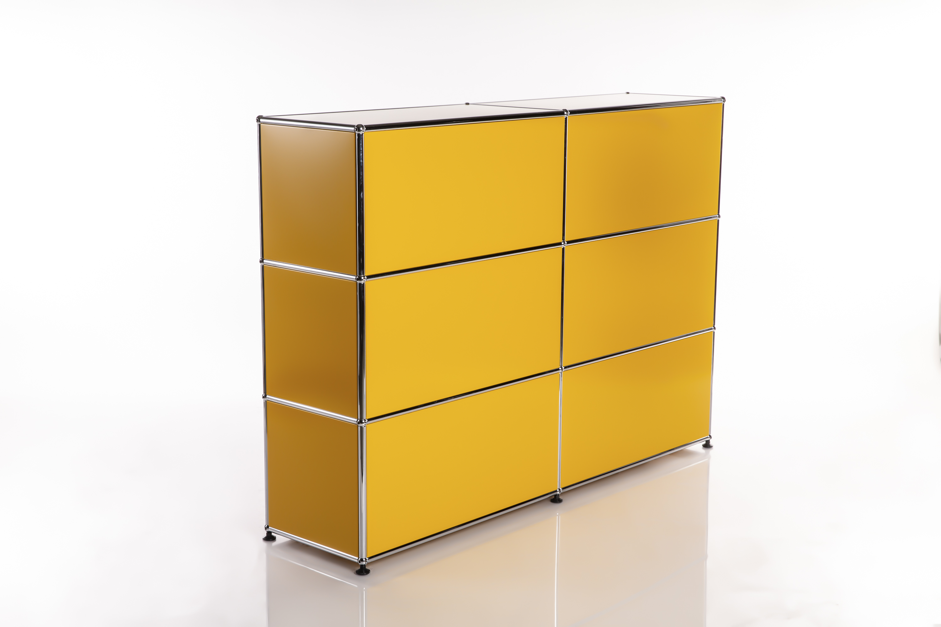 Buffet modulaire jaune vif avec six compartiments rectangulaires (3 rangées, 2 colonnes). Panneaux métalliques jaunes encadrés de tubes chromés brillants. Sur sol clair réfléchissant, fond blanc, vu de face gauche.