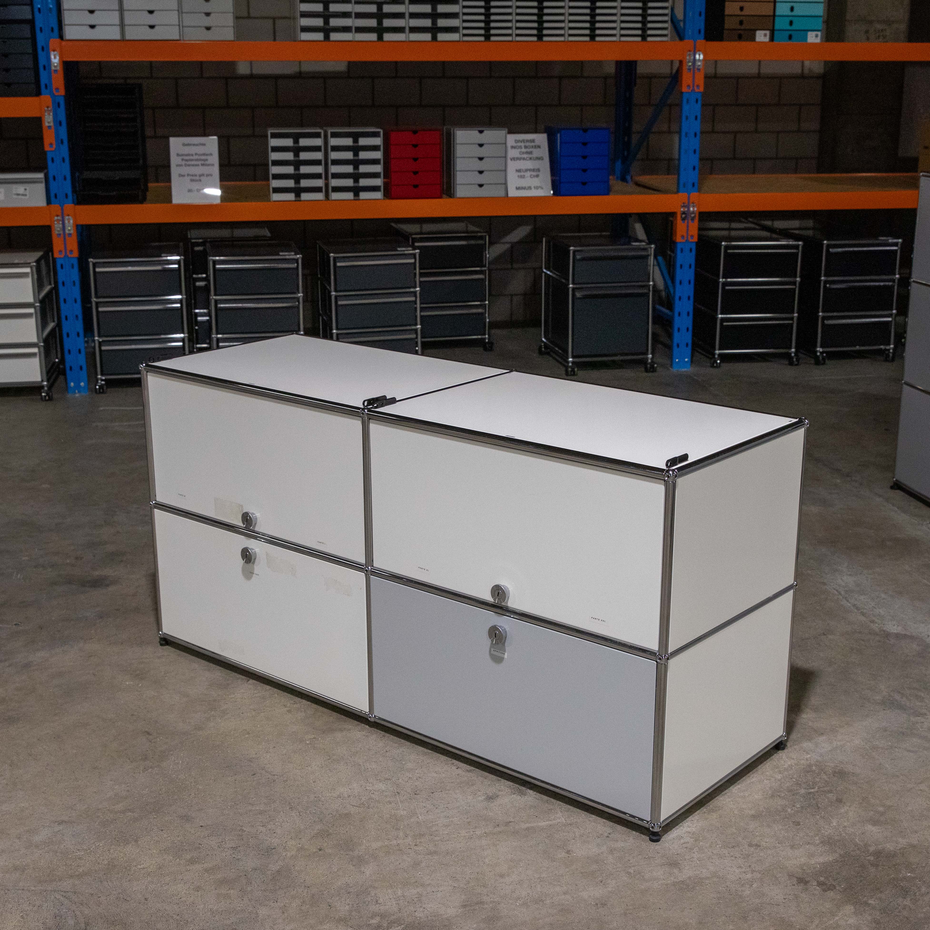 Gebrauchtes USM Haller Regal 2x2, Weiss und Lichtgrau, von vorne. Mit zwei oberen weissen Klapptüren, links zwei weisse Einschübe und rechts unten zwei Klapptüren: eine weiss, eine lichtgrau. Im Lager.