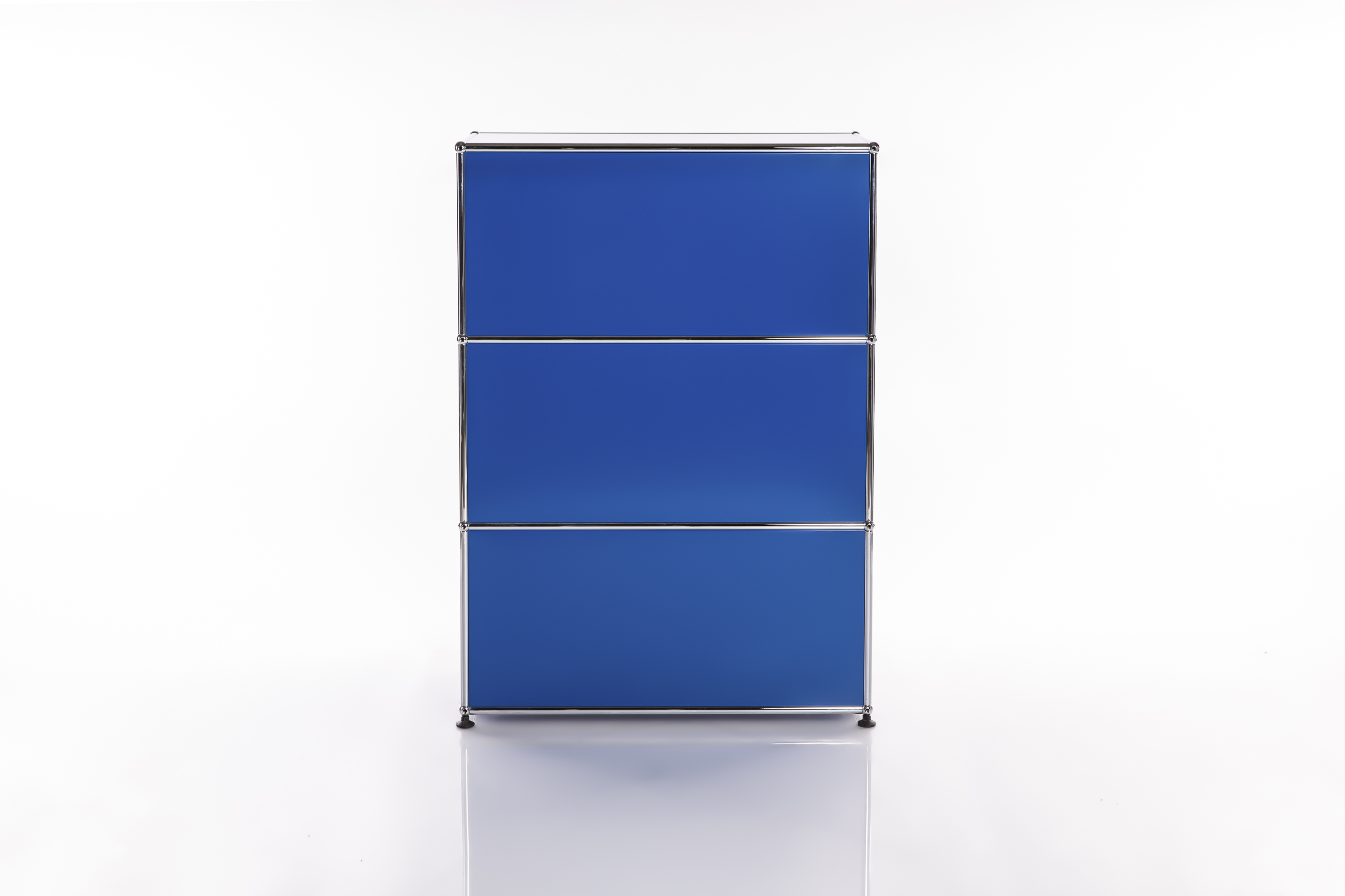 Armadio modulare blu, slanciato e di forma verticale, con tre scomparti sovrapposti. Struttura in metallo cromato lucido su piccoli piedini scuri. Su sfondo bianco chiaro, con riflesso nella parte inferiore.