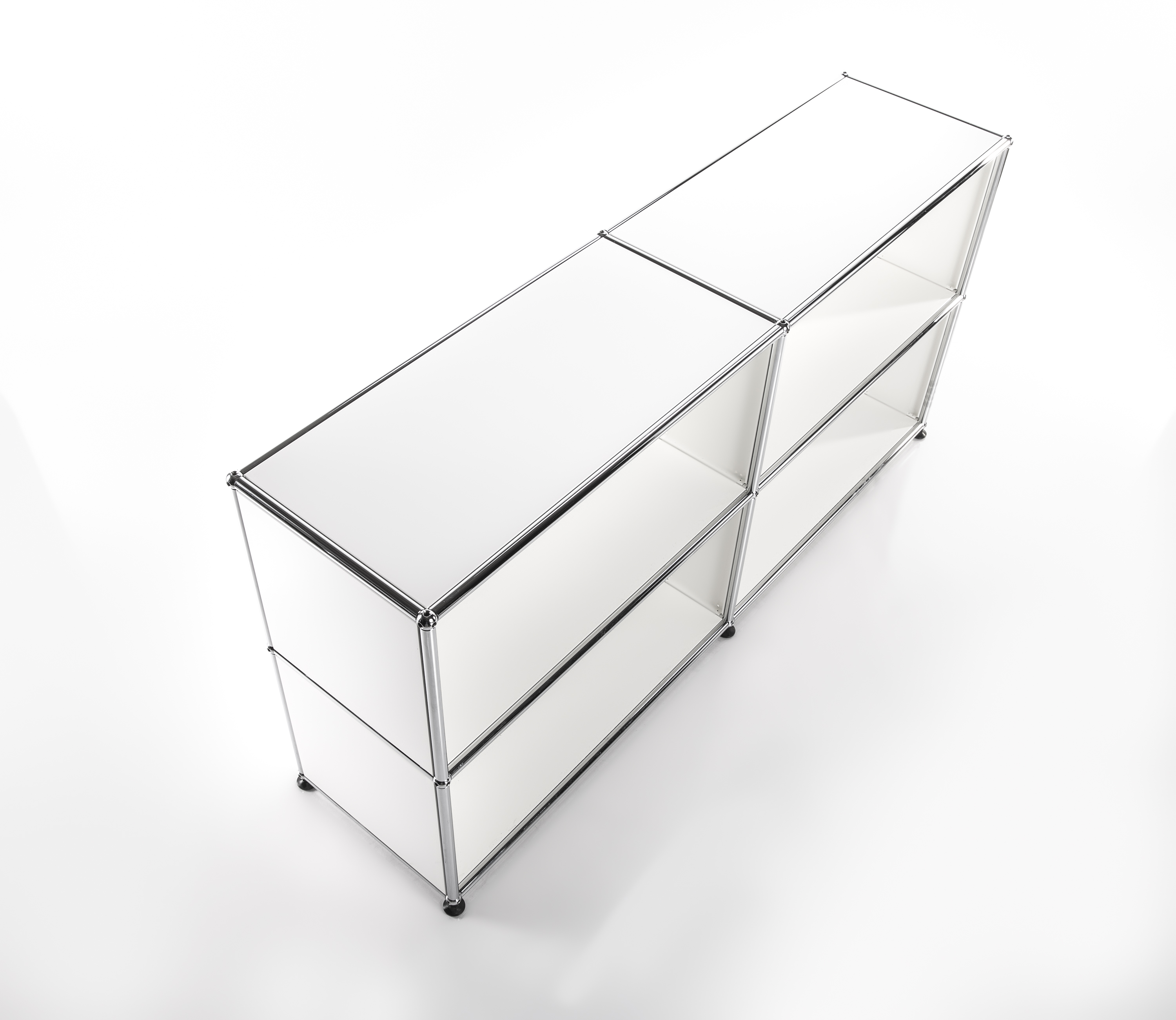 Étagère minimaliste et modulaire blanche, cadre chromé brillant, photographiée en plongée sur fond clair. Deux rangées superposées et trois compartiments côte à côte ; haut fermé, six compartiments bas ouverts.
