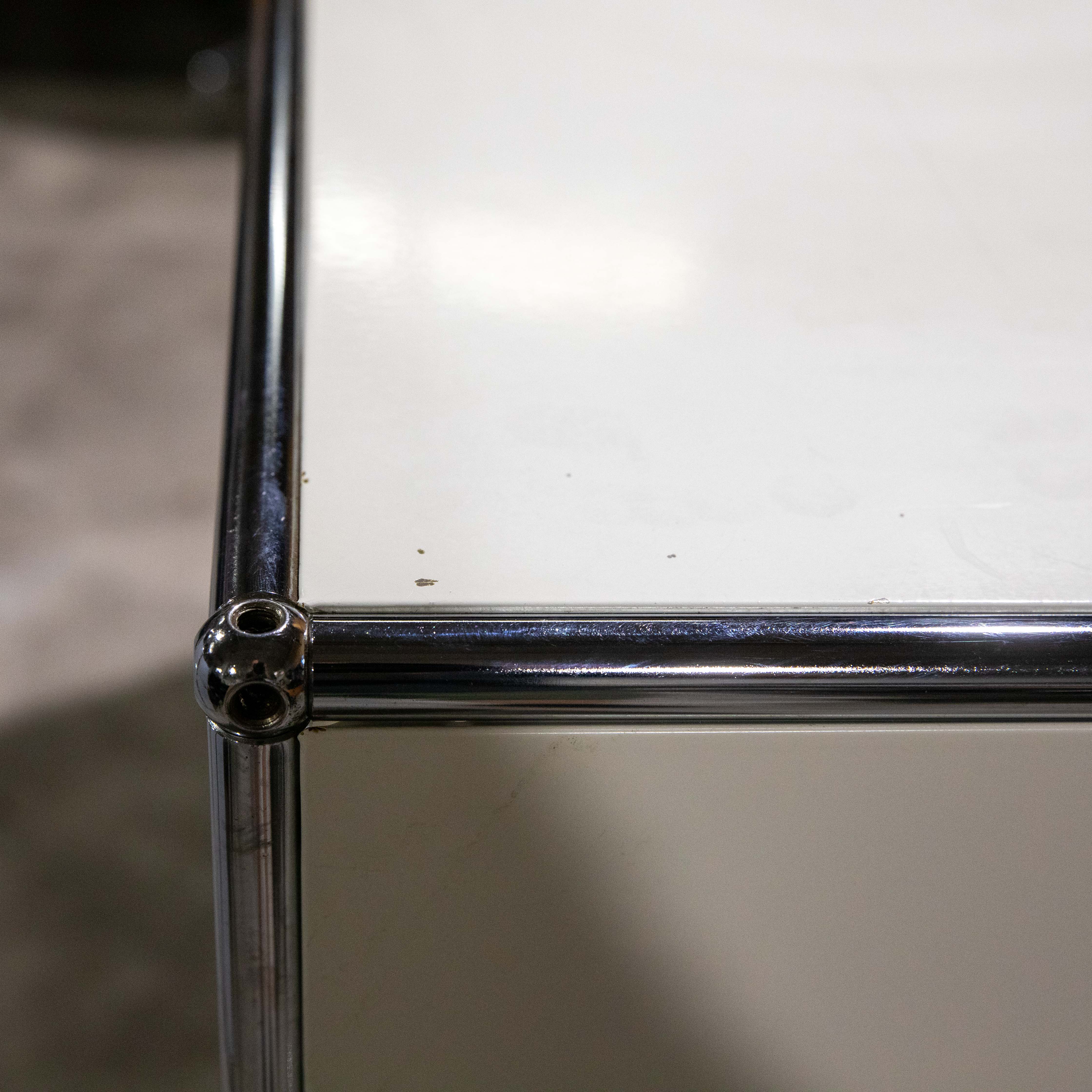 Nahaufnahme der oberen linken Ecke eines modernen modularen Möbelstücks mit glänzend verchromtem Metallrohrrahmen. Kugelverbindung hält vertikale und horizontale Stangen. Glatte cremefarbene Paneele, leichte Spuren, winzige Flecken.