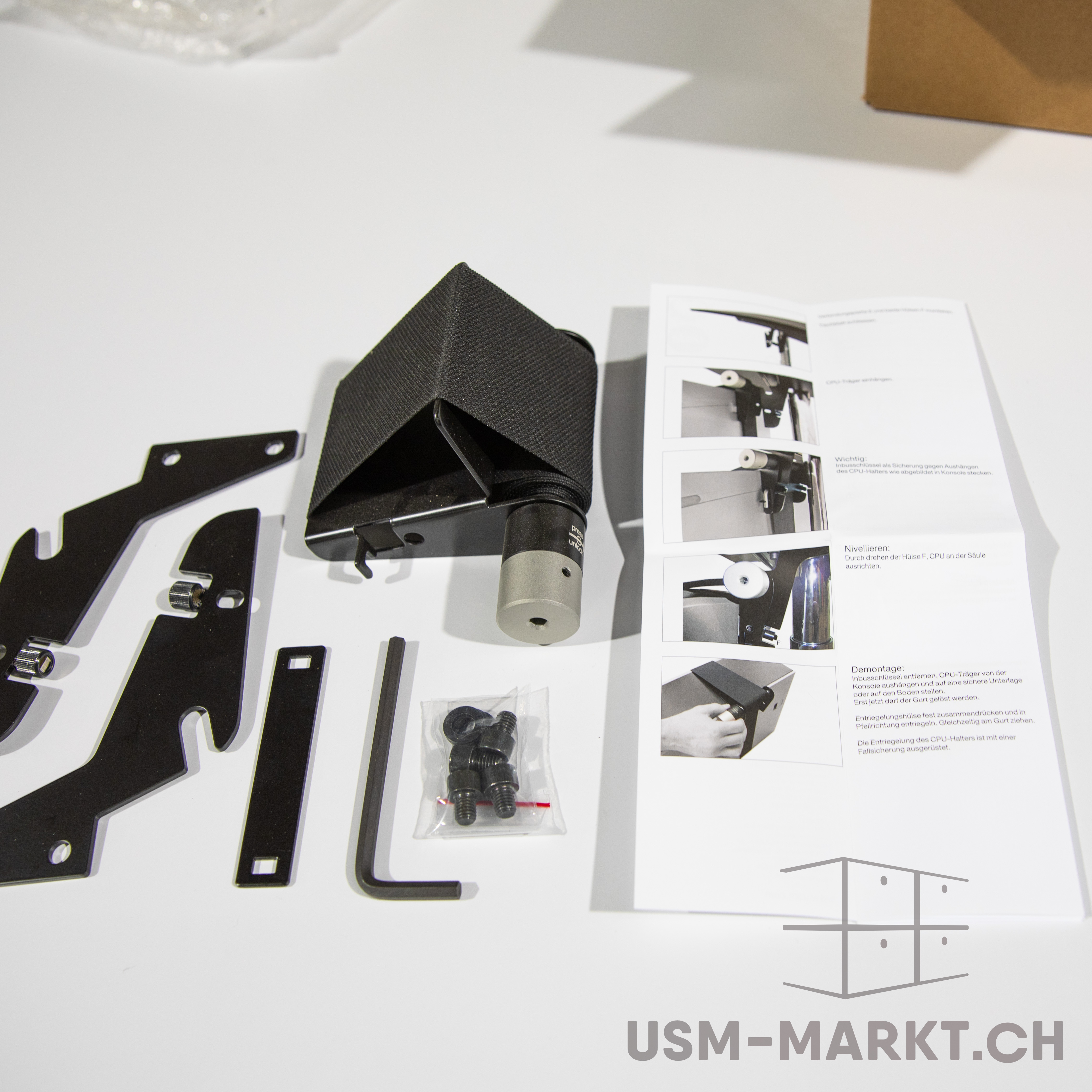 Montagekit für CPU-Halter auf weißem Hintergrund. Bausatz mit schwarz umwickeltem Halterungsarm, schwarzen Metallteilen, Inbusschlüssel und Schrauben. Rechts daneben eine offene Anleitung mit Installationsschritten.