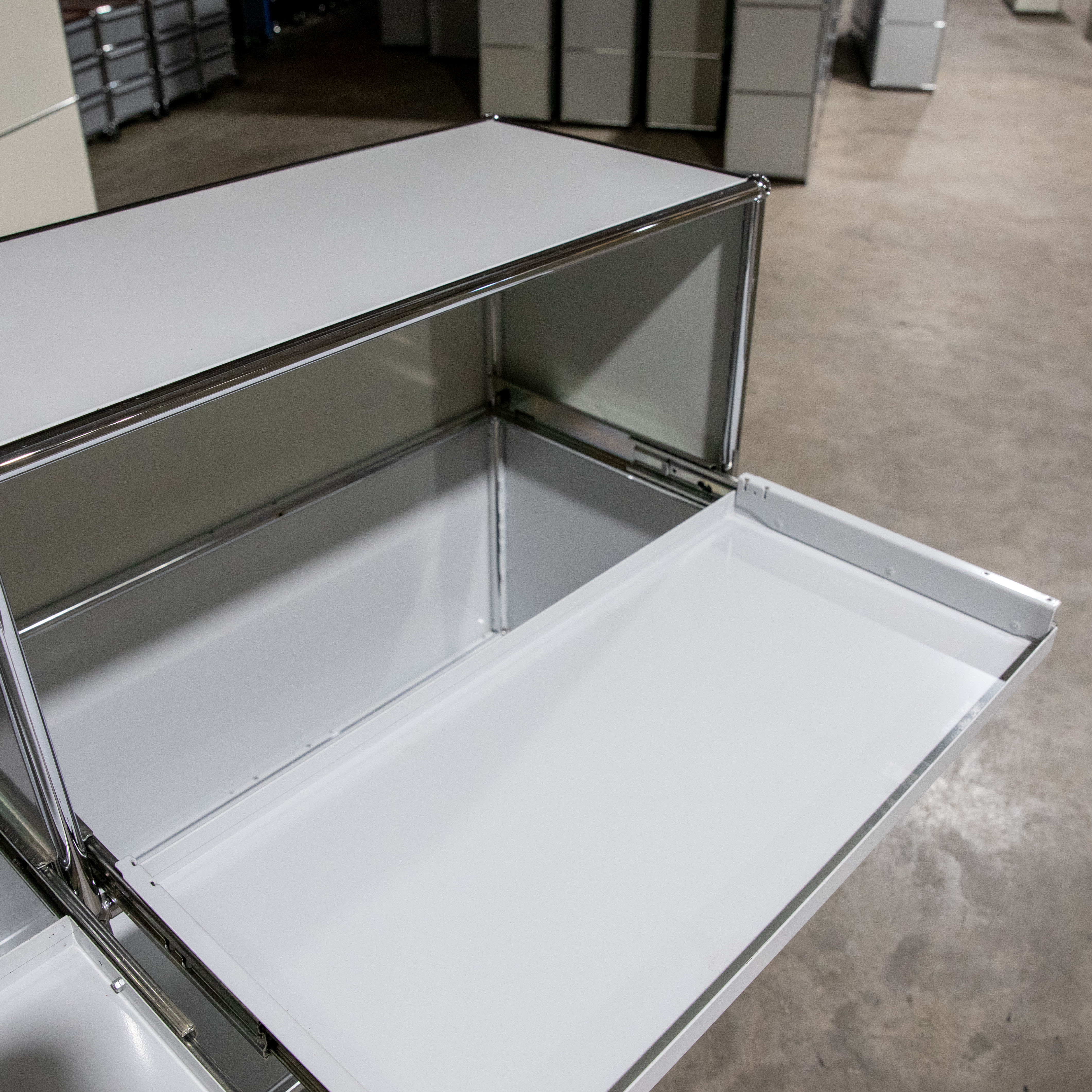 An open, light grey USM Haller module, photographed from slightly above at an angle. A pull-out shelf has been fully extended, revealing its smooth, light grey surface. Inside, silver frames and light grey side panels are visible. Slight signs of wear.