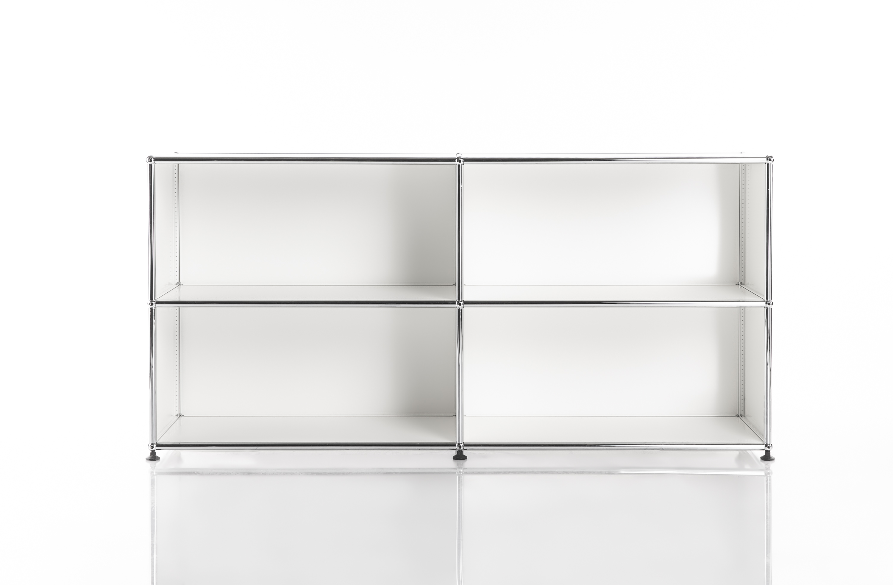 Étagère moderne et modulaire avec cadre en métal chromé brillant, offrant quatre compartiments ouverts blancs en 2 rangées et 2 colonnes. Sur petits pieds noirs, elle se reflète sur les surfaces claires, idéale pour un style minimaliste.