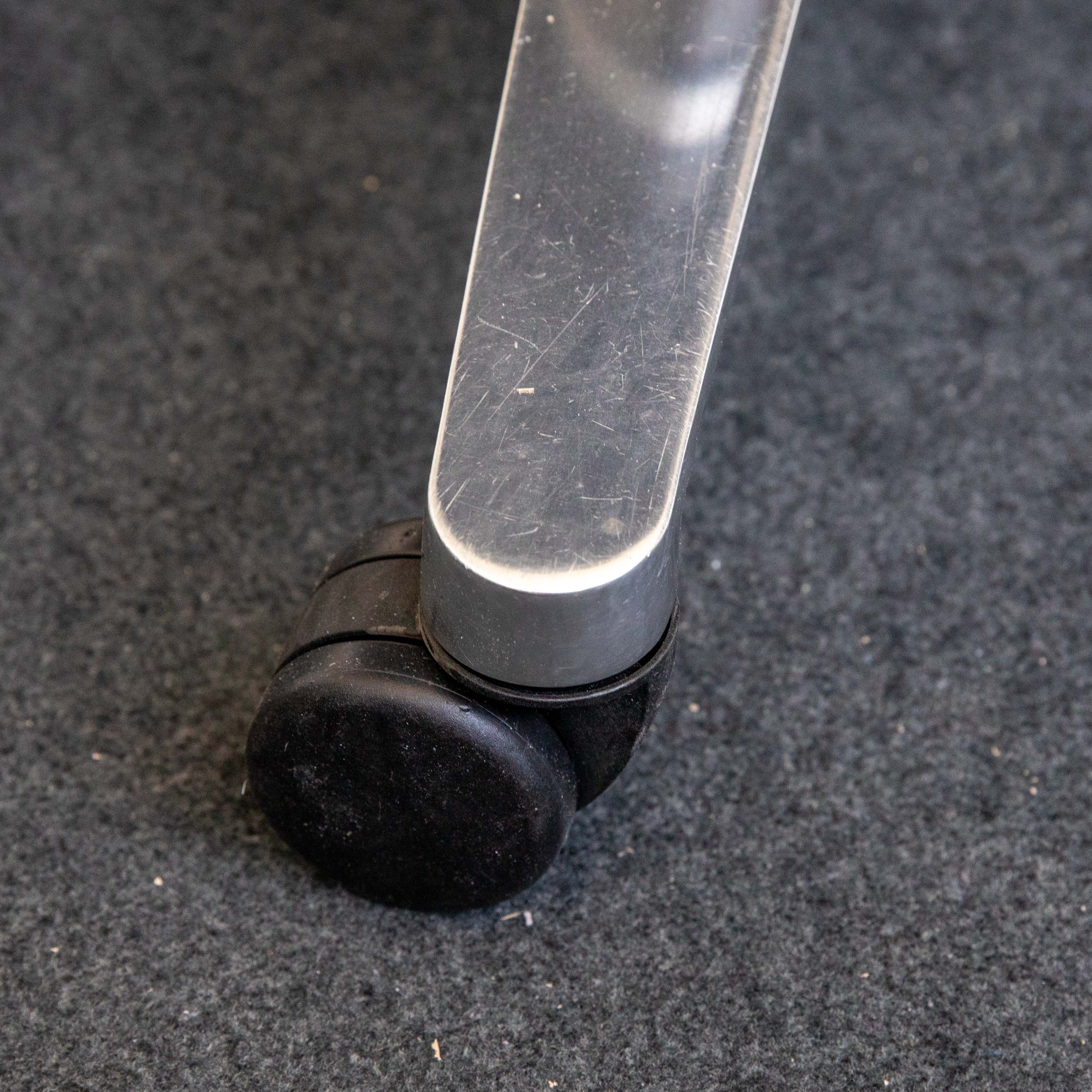 Nahaufnahme einer schwarzen, harten Rolle eines gebrauchten Wilkhahn ON Bürodrehstuhls auf dunklem Teppich. Der silberne Metallfuß zeigt Kratzer und Gebrauchsspuren, die Rolle ist leicht verschmutzt und abgenutzt.