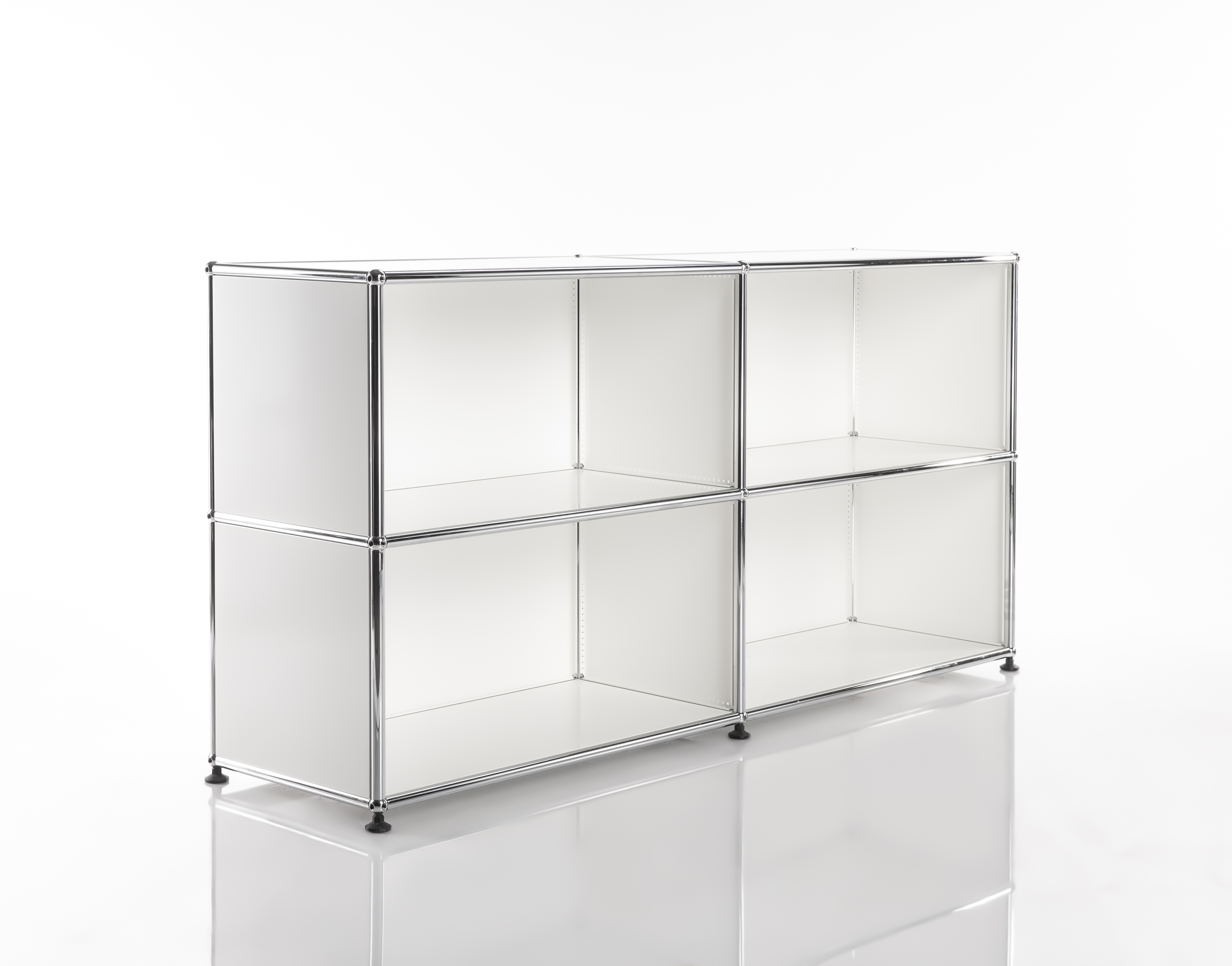 A modern, white modular shelving system featuring glossy, chrome-plated steel tubes. Four open compartments arranged in two rows and two columns on a reflective white surface. Minimalist design with flexible storage options.
