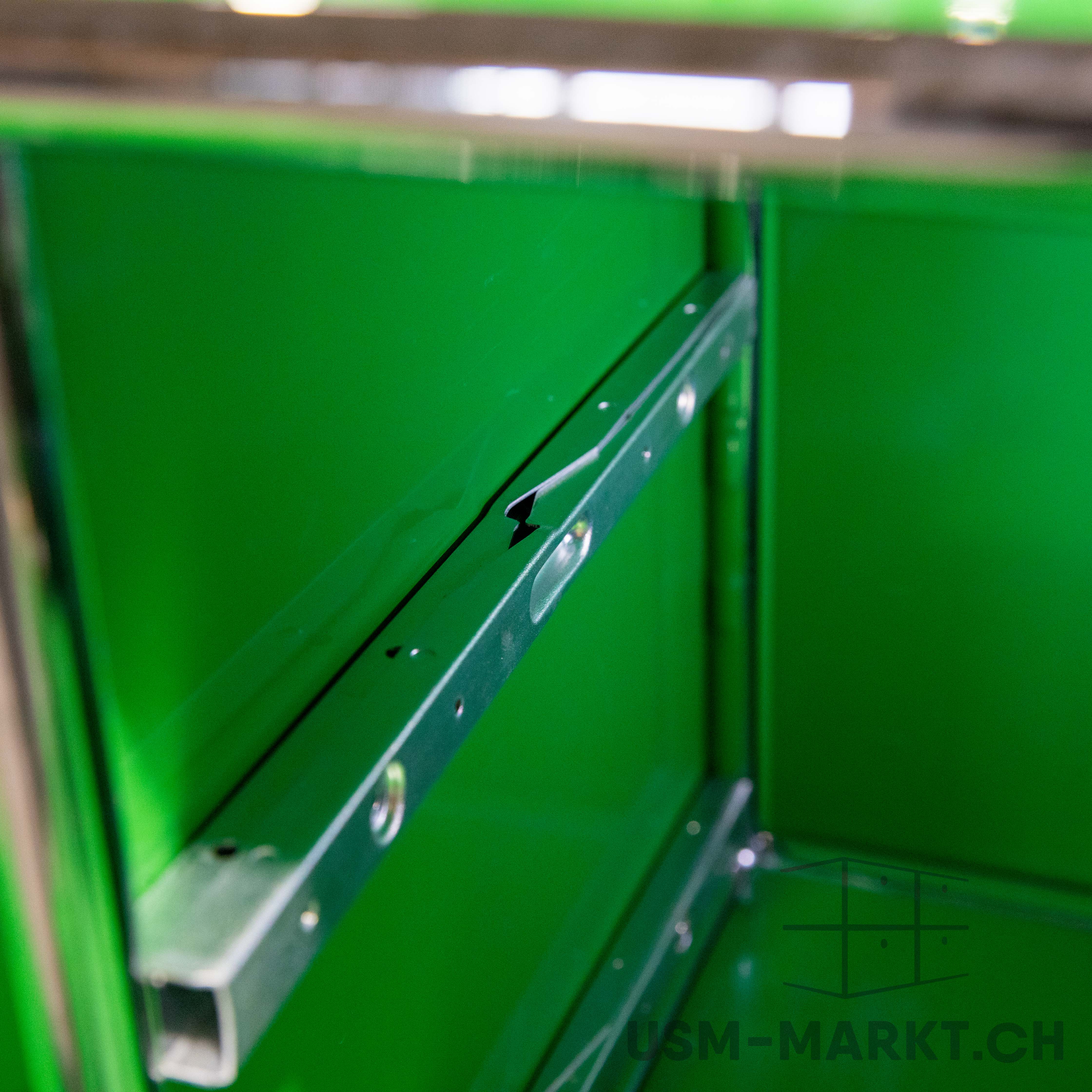 A close-up of the interior of a cupboard or drawer in bright green. The metal side rails for the drawers are visible, mounted on smooth green interior walls. Viewed slightly from above, looking into the depth of the space.