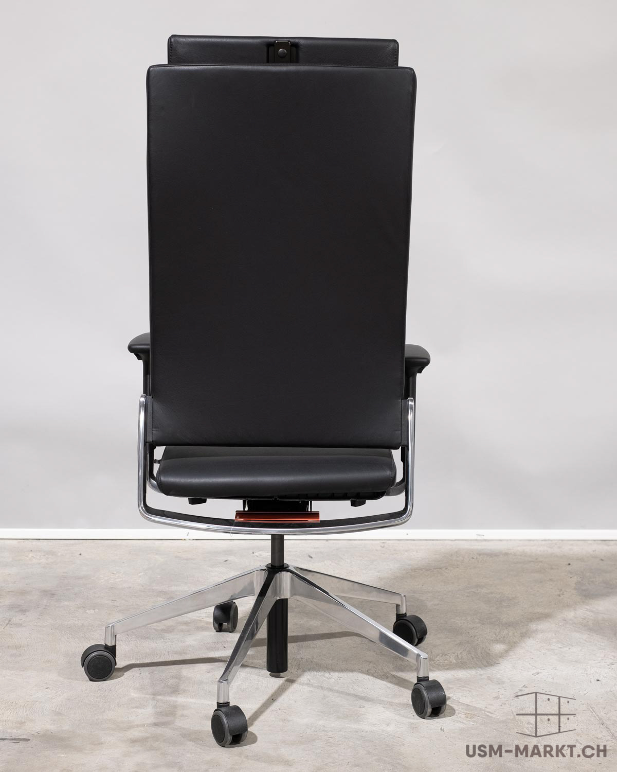 Élégante chaise de bureau noire avec un dossier haut en cuir, vue de dos. Dossier et assise dotés d'un cadre chromé brillant. Piètement à cinq branches en métal poli avec des roulettes noires. Mécanisme rouge apparent.