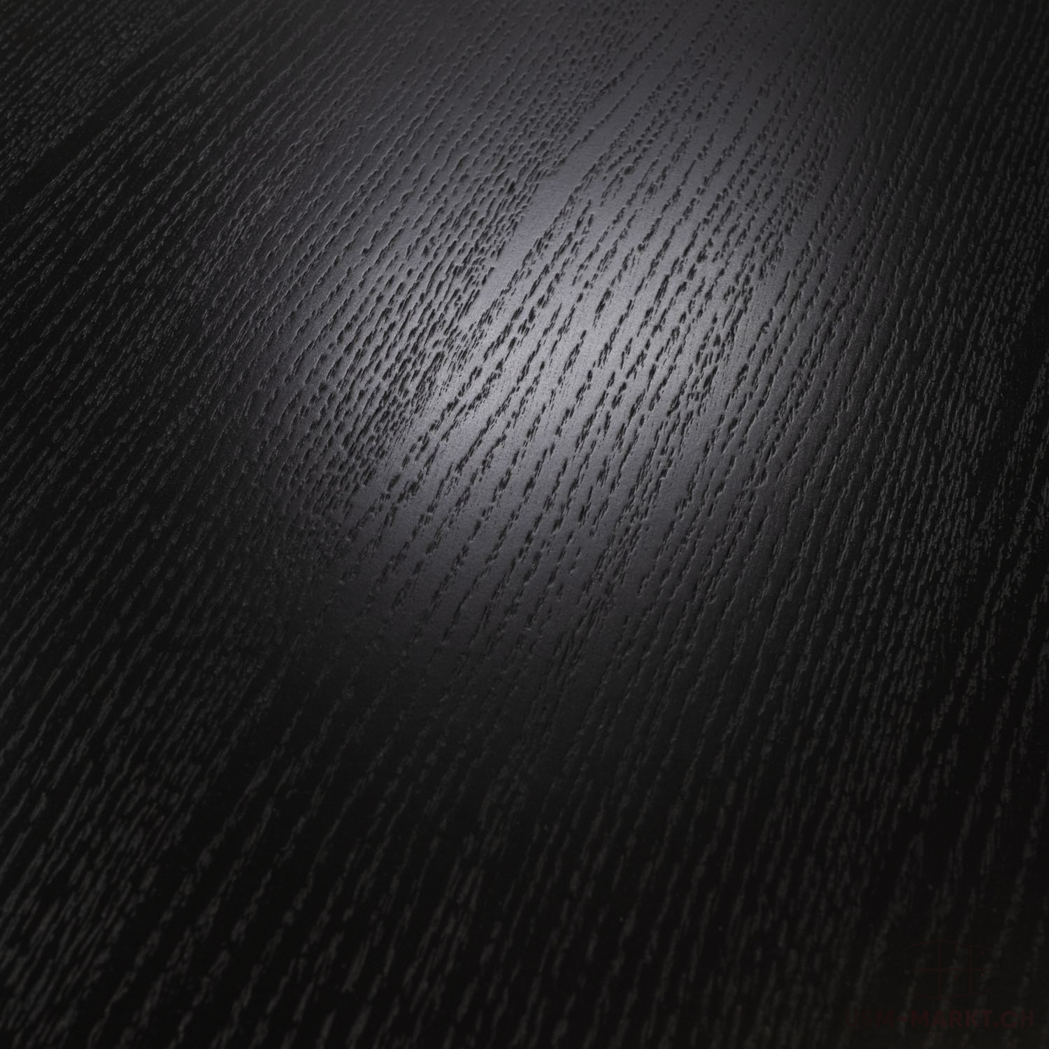 Surface sombre au grain de bois prononcé s'étendant en diagonale. Une légère bande brillante souligne la texture en haut au centre, tandis que le reste paraît plus mat. Couleur du noir profond au gris foncé.