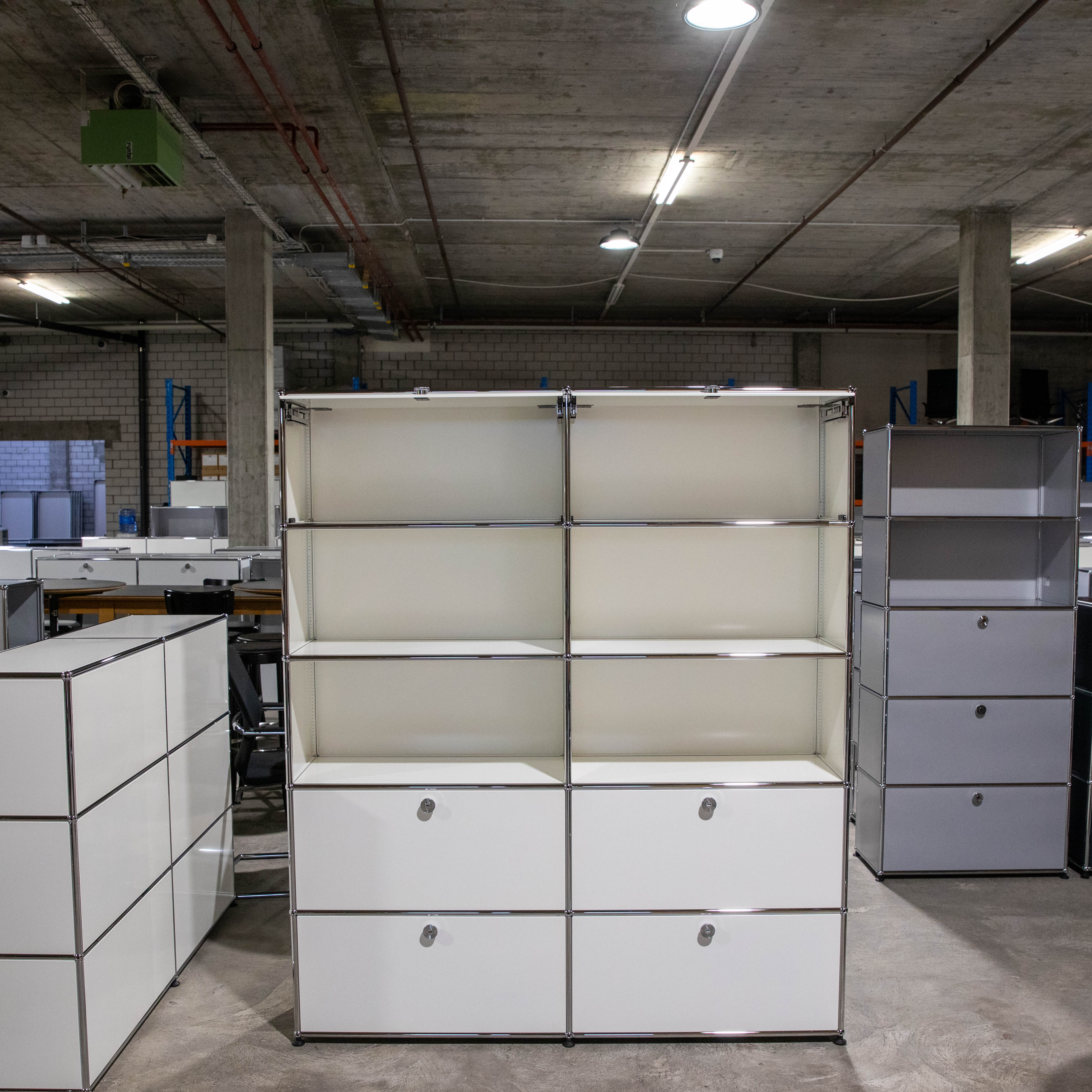 Großes USM Haller Regal in Weiß, modular aufgebaut mit 2 Spalten und 5 Reihen. Oben sechs offene Fächer, unten vier geschlossene Schubladen mit runden Chromgriffen. In industrieller Lagerumgebung.