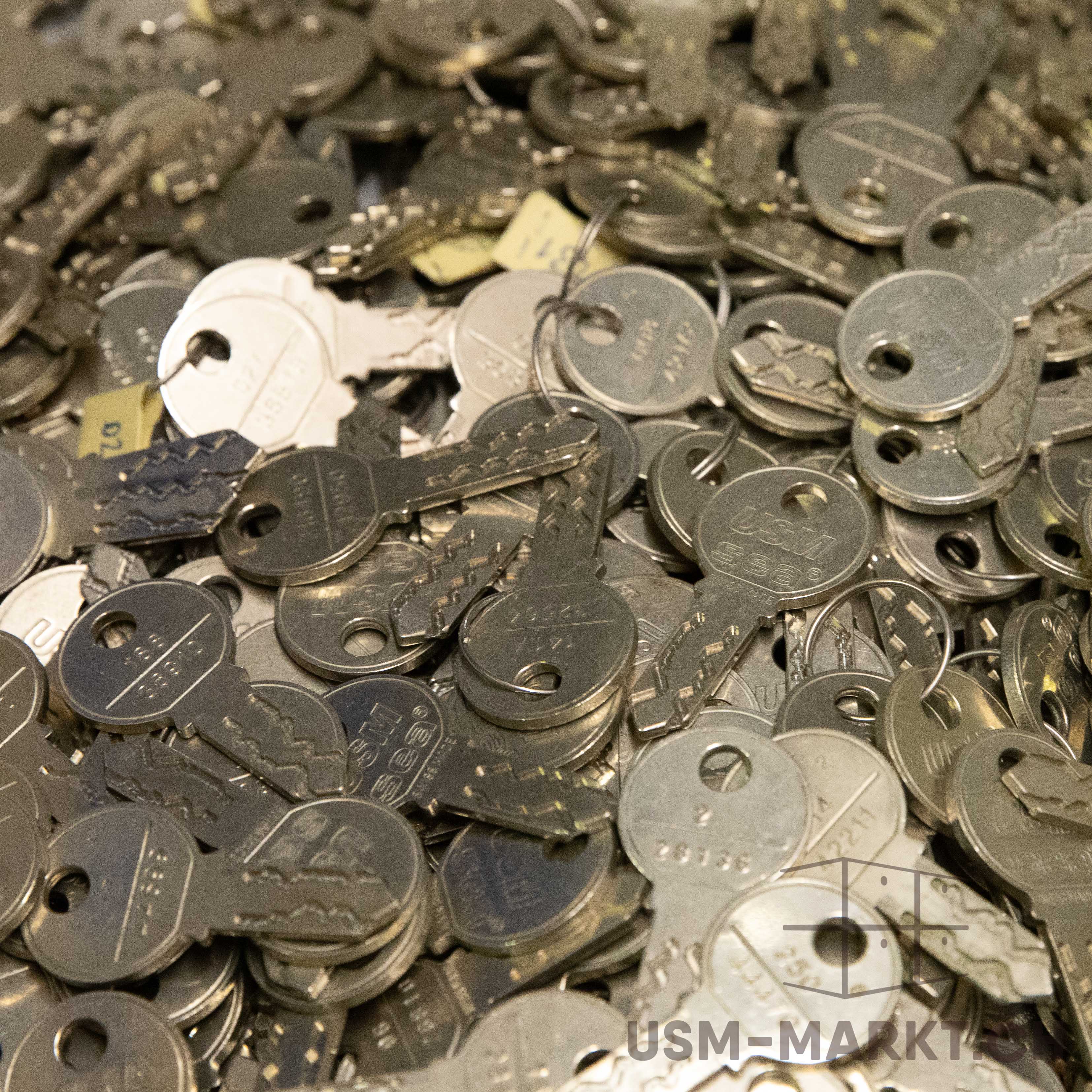 Viele verschiedene Metallschlüssel liegen dicht beieinander und überlappen sich, ihre silbernen, leicht glänzenden Oberflächen füllen das ganze Bildfeld aus. Jeder Schlüssel hat ein rundes oder ovales Kopfende mit Loch und individuelle Zacken.