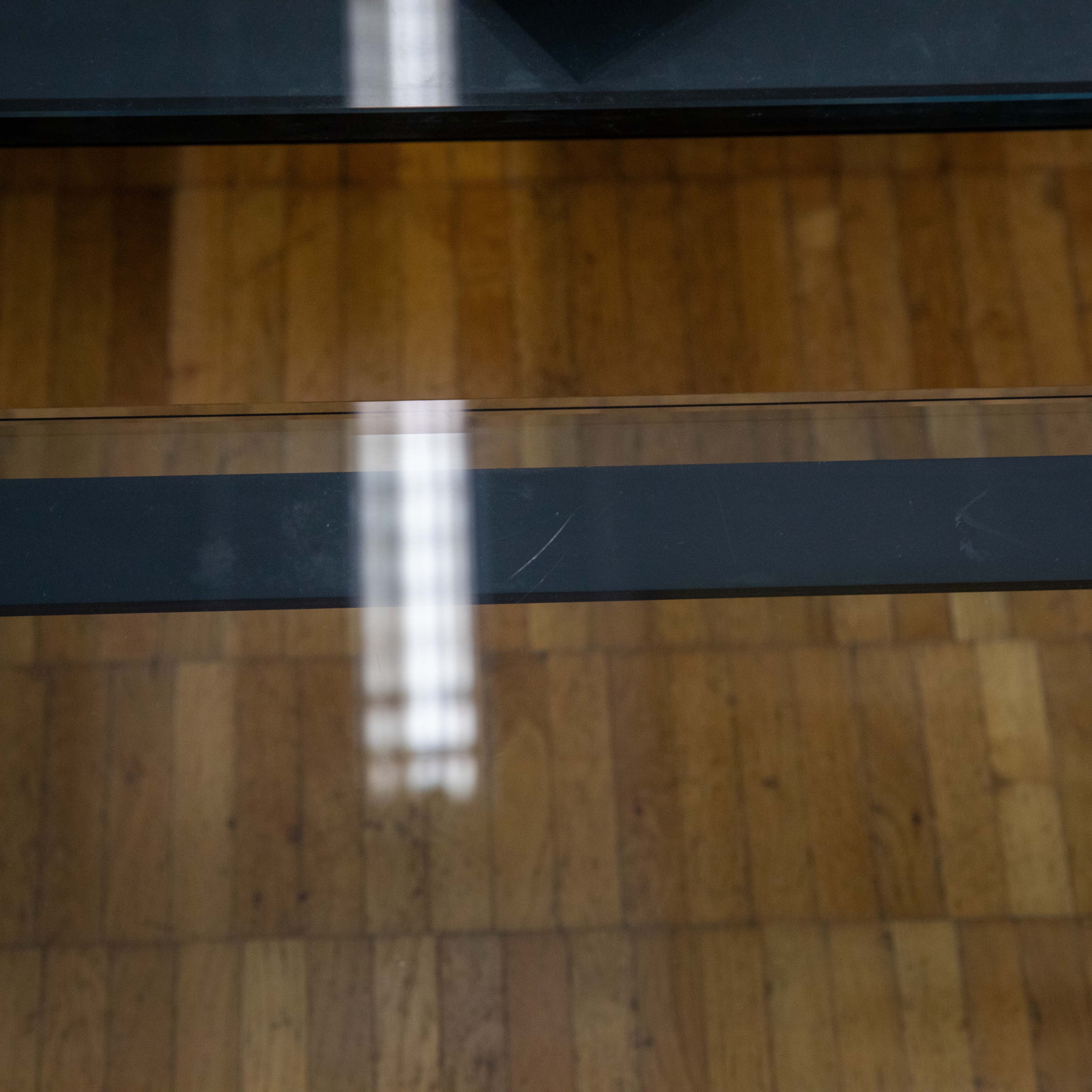 Parquet clair, vu à travers une surface vitrée transparente avec une bande horizontale foncée au centre. Plusieurs reflets lumineux verticaux et clairs sur la surface vitrée, avec une zone sombre floue en haut.