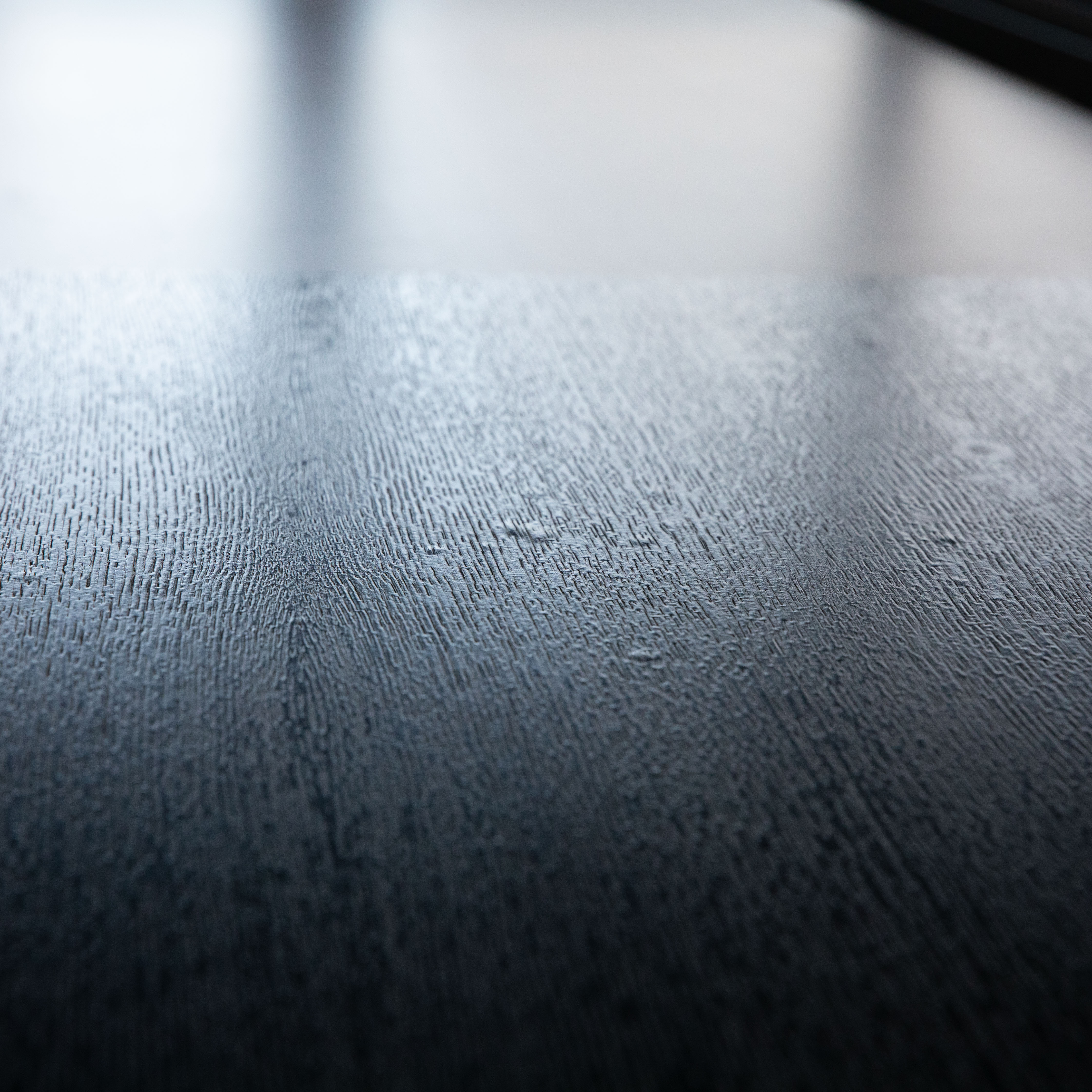 Close-up of the black, lacquered oak surface of a USM Haller table. The fine, slightly raised grain is clearly visible and catches ambient light in subtle reflections. Low, oblique angle.