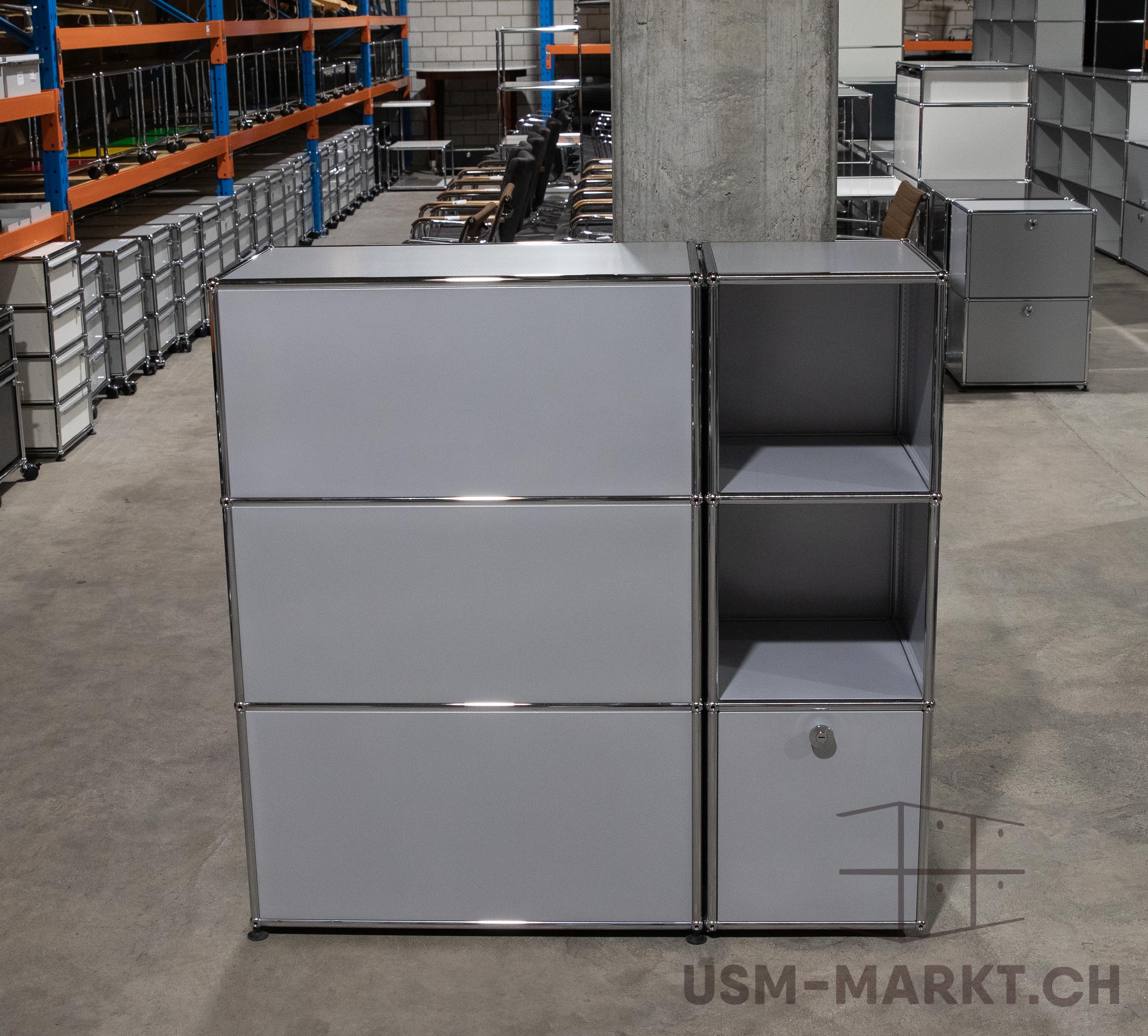 Modulares Regal-/Schranksystem 3x3. Oben links zwei geschlossene Spalten, rechts offene Fächer. Unterstes Fach rechts mit Schloss. Steht auf grauem Betonboden in Lagerhalle. Im Hintergrund weitere Regale und Büromöbel.