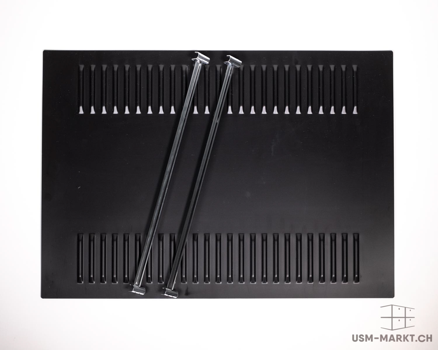 A rectangular black metal plate with two rows of vertical slits along the top and bottom edges. Two shiny silver metal rods lie diagonally across it, with flat T-shaped ends; they cross slightly in the centre.