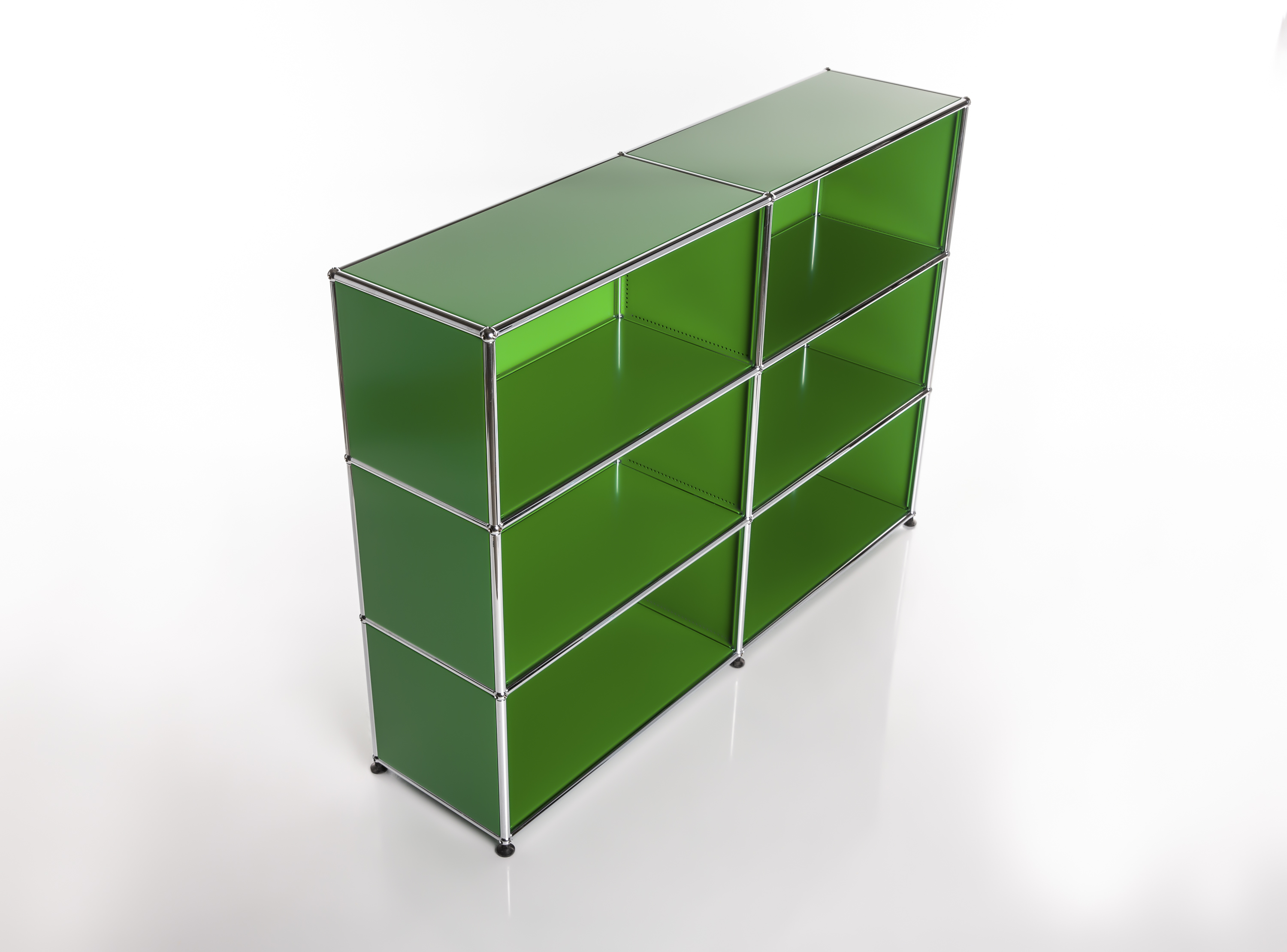 A modern modular shelving unit comprising six bright green compartments with polished chrome frames, arranged in three rows and two columns, stands on a light-coloured, reflective base. The clean layout emphasises the timeless design of the shelving unit.