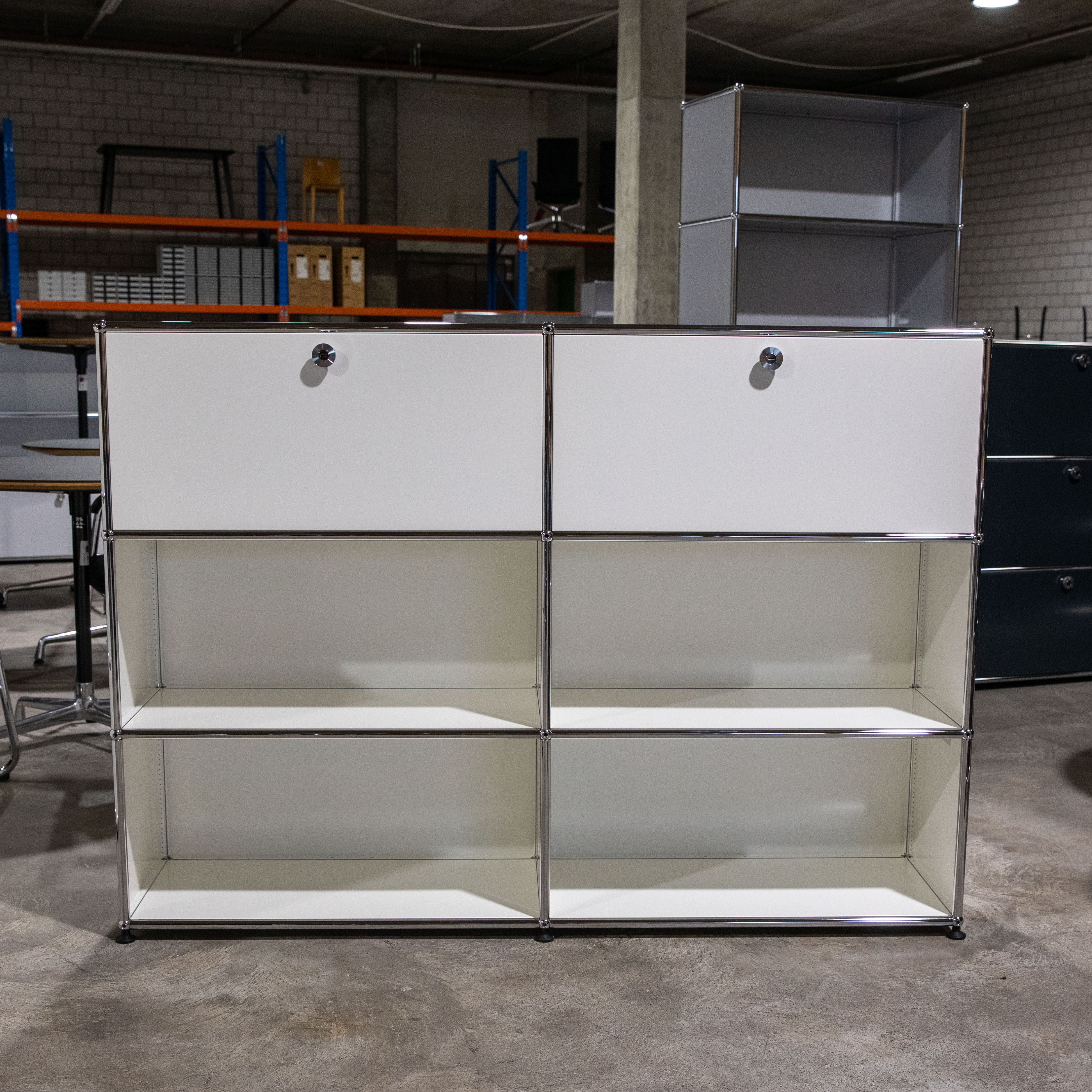 Weisses USM Haller Regal, 2x3 Module. Oben zwei geschlossene Fächer mit Klapptüren und verchromten Griffen. Darunter je zwei Reihen mit zwei offenen Ablagefächern. Aus weissen Metallplatten und Chromstangen gefertigt.