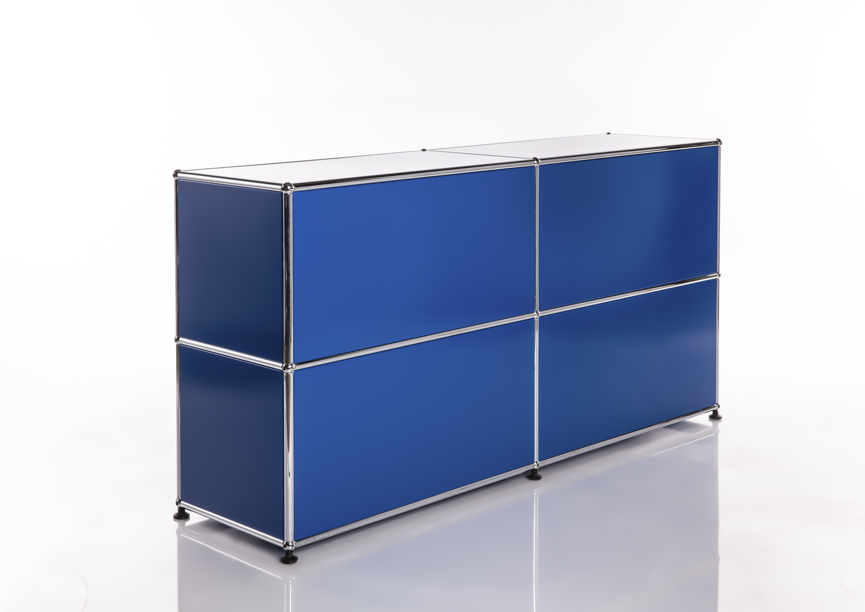 Buffet modulaire moderne, de couleur bleu vif, avec une structure chromée brillante. Quatre compartiments rectangulaires disposés sur deux rangées. Dessus blanc, façades et côtés bleu foncé. Reposant sur de petits pieds noirs, sur fond clair avec reflets.