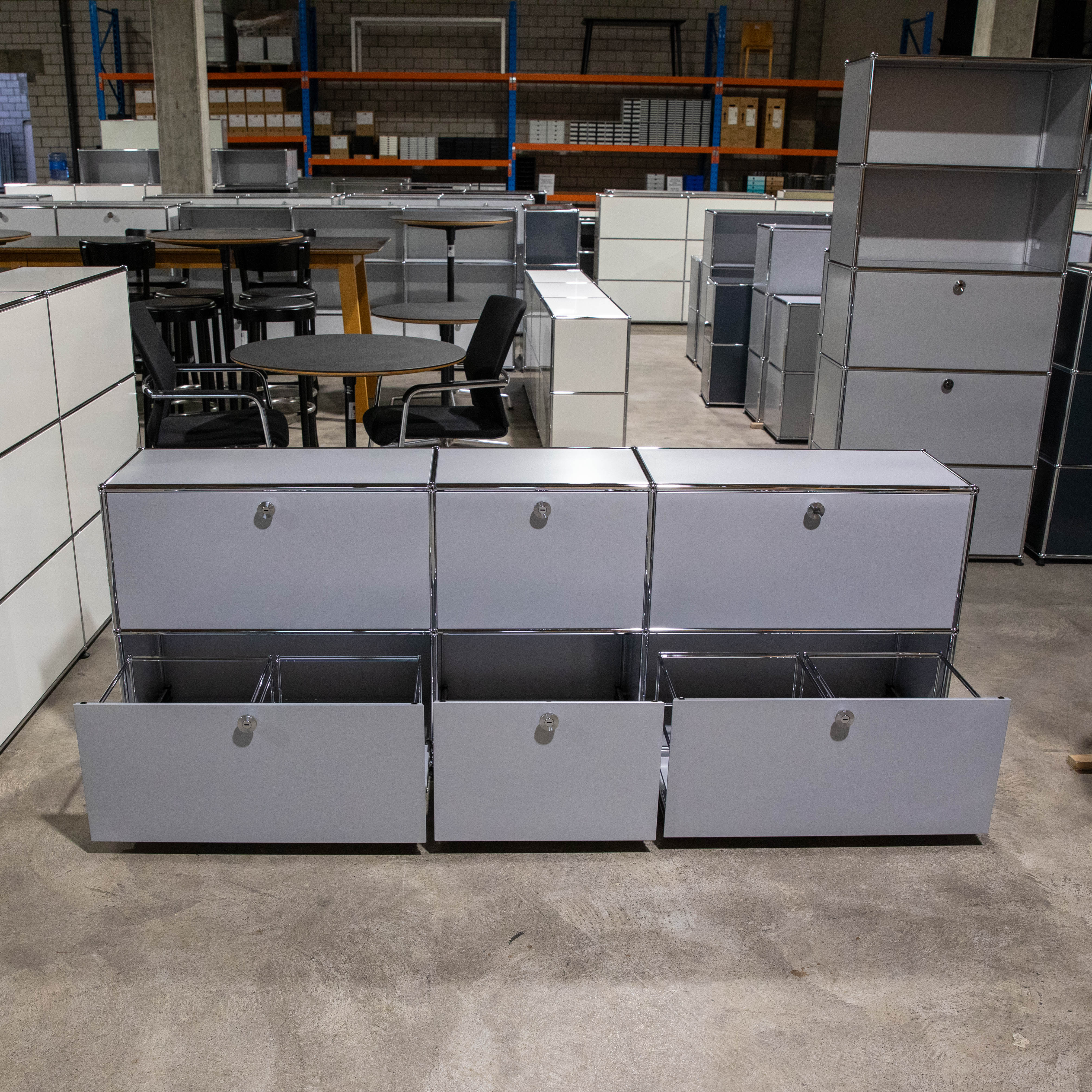 Mattsilbernes USM Haller Sideboard 3x2 zentral. Oben drei geschlossene Fächer mit Schlüsselschlössern. Unten drei ausgezogene Schubladen: außen Hängeregisterrahmen, Mitte leer. Im Hintergrund USM Möbel/Tische.