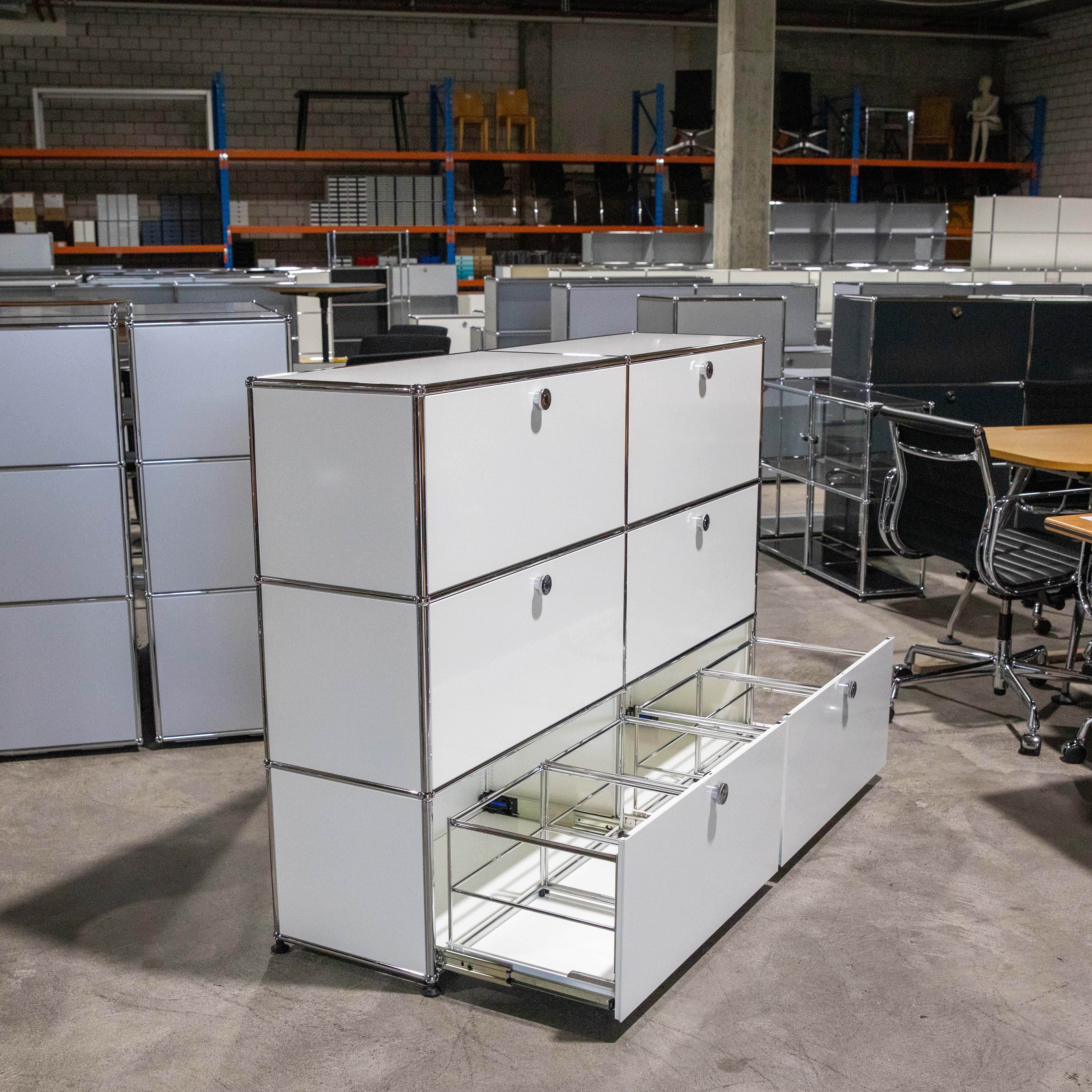 Weisses USM Haller Regal mit 2 breiten und 3 hohen Fächern. Unten ist eine Schublade offen mit Hängeregistratur, die anderen 5 Fächer sind geschlossen. Modulares Möbel mit verchromten Verbindern, im Lagerraum.